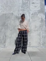 Pantalón de corte holgado y silueta tipo barrel, confeccionado en tela viyela con estampado de cuadrillé en tonos negro, beige y líneas finas rojizas. Presenta cintura elástica y puños ajustados en el tobillo.