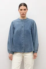 Camisa de jean de corte clásico con cuello mao, cierre frontal con botones y mangas largas abullonadas con puños elásticos.