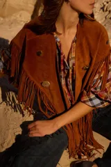 Chall de gamuza natural con diseño de flecos largos en los bordes y detalle de pins metálicos en la parte frontal.