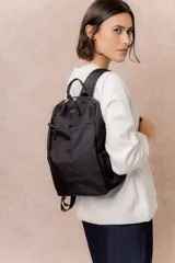 Mochila negra de diseño minimalista y compacto, con compartimento principal con cierre, bolsillo frontal con cierre oculto, bolsillos laterales y tiras regulables. Incluye logo metálico de la marca.
