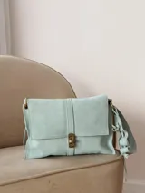 Bandolera de cuero color beige claro, con solapa frontal, cierre metálico de broche y correa regulable con detalles ondulados.