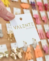 Aros tipo argolla pequeña con diseño en forma de corazón, combinando metal dorado con esmalte color crema.