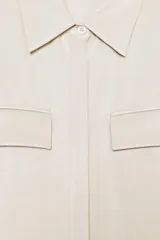 Camisa de cuello solapa y manga corta, confeccionada en tejido satinado. Presenta falsos bolsillos con solapa en el delantero, bajo asimétrico y cierre frontal con botones.