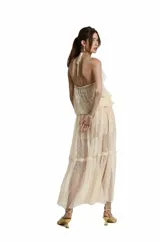 Vestido largo de encaje color beige, con escote en V y tirantes finos tipo halter. Presenta volantes en la parte superior y falda fluida con sutiles transparencias.