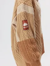 Cardigan oversize de tejido de punto grueso con diseño de bloques de color en tonos tierra. Presenta cuello en V, cierre frontal con botones, mangas largas con terminación abullonada y parches decorativos en el pecho y hombro.