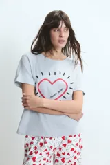 Pijama compuesto por una remera gris de manga corta con estampa frontal de corazón y un pantalón largo blanco con estampado de corazones rojos.