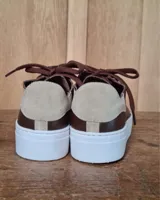 Zapatilla urbana de cuero con diseño combinado en color dorado metalizado y gamuza en tono tostado. Presenta cordones al tono, suela de goma blanca y detalles en cuero marrón en la parte posterior.