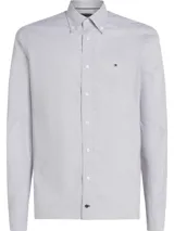Camisa de vestir Tommy Hilfiger de corte clásico, confeccionada en tejido Oxford de algodón regenerativo con estampado a cuadros Tattersall en tonos blanco, azul y gris. Tiene cuello abotonado, cierre con botones, manga larga y logo bordado en el pecho.