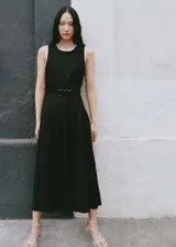 Vestido midi negro sin mangas, con cuello redondo, cinturón con hebilla y falda evasé con pliegues. Presenta cierre lateral con cremallera y botón en la parte posterior.
