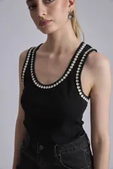 Remera negra sin mangas, tipo musculosa, con escote redondo y ribetes blancos con apliques de perlas en el contorno del cuello y las sisas.