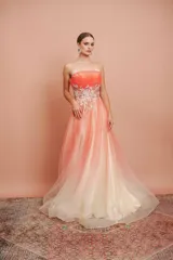 Vestido largo de fiesta, strapless, con busto drapeado y falda de tul con degradé de color coral a blanco. Presenta bordados florales en el corpiño.