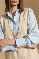 Chaleco tejido color azul, con escote en V, cierre frontal con botones y diseño de líneas verticales en relieve. Presenta terminaciones acanaladas en el ruedo y un borde ondulado en el escote.