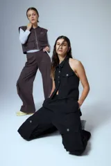 Chaleco de denim negro con escote halter, cuello camisero y cierre frontal con botones metálicos. Presenta dos bolsillos frontales con solapa y diseño sin mangas.
