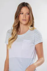 Remera de manga corta con cuello redondo y bolsillo frontal. Presenta un diseño de bloques de color y rayas horizontales: la parte superior (hombros y mangas) tiene rayas finas amarillas, grises y celestes; la parte media es blanca jaspeada con un bolsillo; y la parte inferior es gris jaspeada.