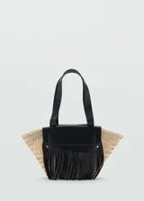 Bolso de mano tipo cesta confeccionado en tejido de fibra natural, con detalles en cuero negro que incluyen doble asa corta, solapa frontal y flecos decorativos.