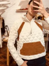 Sweater blanco con diseño acolchado, cierre parcial con cremallera, detalles en cuero color marrón y bolsillo tipo parche en el frente.