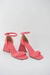 Sandalias de tacón color rosa coral, con punta cuadrada, tira delgada sobre los dedos y pulsera tobillera con hebilla. El tacón es geométrico y tiene una altura media.