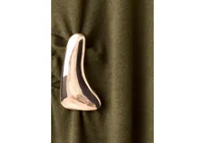 Vestido largo de punto en color verde oliva, con cuello alto y manga larga. Presenta un diseño ajustado en la parte superior que se extiende hacia una falda recta, con un detalle metálico decorativo en el lateral de la cintura.