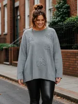 Buzo de hilo color marrón, de corte oversize y cuello redondo, con detalles de flores en relieve bordadas en la parte frontal.