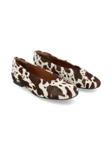 Ballerinas planas confeccionadas en cuero con pelo con estampado animal print de vaca en tonos marrón y blanco, con suela fina y talón cerrado.