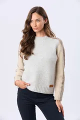 Buzo tejido de abrigo con cuello redondo y manga larga. Presenta un diseño de bloques de color en tonos gris claro y beige.