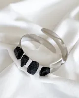 Brazalete rígido plateado con cuatro piedras de turmalina negra incrustadas.