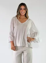 Blusa de algodón color celeste, con cuello en V con detalles desflecados y mangas largas acampanadas con volados escalonados.