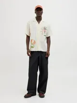 Camisa de manga corta color crema con estampado de flores y hojas en tonos naranja y verde. Tiene cuello resort, cierre frontal con botones y calce relajado.