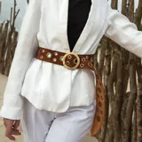 Cinto marrón de gamuza con hebilla circular dorada y ojalillos metálicos.
