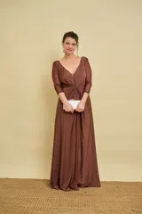 Vestido largo color marrón de silueta fluida, con escote en V pronunciado, mangas tres cuartos de tul con detalles sutiles, nudo drapeado en el centro del pecho y tajo delantero en la falda.