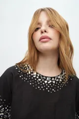 Blusa blanca de manga corta con cuello redondo y bordado de lentejuelas y mostacillas plateadas en el cuello y las mangas.