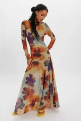 Vestido largo de tul con estampado floral en tonos marrones, naranjas y violetas, de manga larga y silueta fluida.