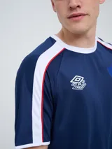 Remera deportiva de entrenamiento Umbro del Club Nacional de Football, color azul marino con detalles en blanco y líneas rojas en los hombros. Cuenta con el logo de la marca y el escudo del club en el pecho.