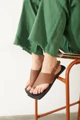 Sandalias de cuero color marrón con diseño de dedo, tira ajustable en el talón y suela plana de color negro.