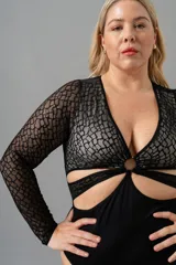 Body negro de encaje elastizado con mangas largas y transparencias. Busto forrado en LYCRA® color crudo, aro en el escote y broches en la entrepierna con fundillo de algodón.