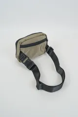 Bandolera color gris con cierre principal y bolsillo frontal con cierre. Cuenta con correa ajustable negra y hebillas de plástico.