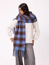 Bufanda de tejido suave con diseño de cuadros grandes en tonos azul y marrón, con flecos en los extremos y etiqueta de la marca Rusty.