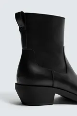 Bota estilo cowboy de caña media, color negro, con punta cuadrada, tacón bajo y cierre lateral.