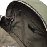 Mochila urbana de diseño compacto en color verde militar, confeccionada en material textil. Presenta un compartimento principal con cierre, un bolsillo frontal con cierre y detalles de tiradores de cuerda trenzada en blanco y negro. Incluye el logo de la marca XL Extra Large en un aplique circular metálico en la parte inferior.