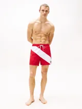 Short de baño rojo con cintura elástica ajustable con cordón, corte amplio y logo de Tommy Hilfiger en la pierna. Presenta una franja diagonal blanca con el logo de la marca en la parte inferior.