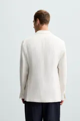 Blazer color crudo de lino y algodón, corte regular, con cuello de solapa de pico, manga larga con puños abotonados, bolsillos de vivo en el pecho y bolsillos de solapa en la cadera, bolsillo interior, aberturas en la espalda y cierre frontal cruzado con botones.