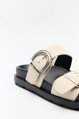 Sandalia tipo slide color tostado, con doble tira ancha y hebillas metálicas plateadas con diseño texturado. Su base es ergonómica y liviana, de color negro.