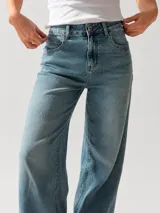 Pantalón de jean con corte wide leg y tiro medio-alto. Presenta un lavado gris azulado desgastado con acabado vintage y ruedo desflecado.
