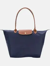 Bolso tipo tote de nylon azul marino con manijas y solapa frontal en cuero sintético marrón. Cuenta con cierre de solapa con botón a presión y cierre principal superior.