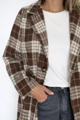 Chaqueta larga de corte recto con estampado de cuadros en tonos marrones y beige. Presenta cuello con solapas, cierre frontal con un botón y bolsillos laterales funcionales. Incluye forro interior.