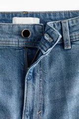 Jean de denim de algodón con leve stretch, tiro alto y piernas amplias de corte holgado. Presenta bolsillos traseros de parche, cierre con botón y pliegues en la parte delantera y trasera.