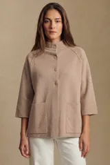 Cardigan de punto color beige, con cuello alto, cierre frontal de botones y mangas tres cuartos. Presenta dos bolsillos frontales y un corte holgado.