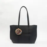 Cartera tipo tote bag de color negro con textura granulada, cuenta con doble asa de hombro y un monedero circular colgante con estampado animal print.