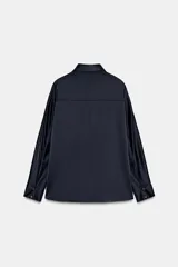 Camisa de manga larga confeccionada en tejido satinado, con cuello solapa, cierre frontal con botones y bajo asimétrico.