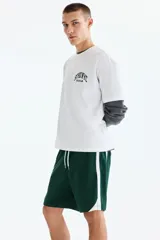 Short deportivo de color verde oscuro, confeccionado en nylon, con bandas laterales blancas, cintura elástica ajustable mediante cordón blanco y corte estándar.